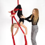 A student receives assistance from a talented trainer in how to hold their body for an inverted silks trick. Roundabout Circus in Wyoming New South Wales offers classes on aerial apparatus like silks, lyra and static trapeze.